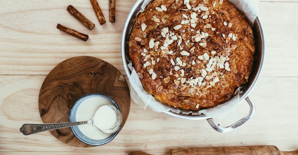 Overhead view of almond-topped cake with cinnamon and cream on a wooden table.