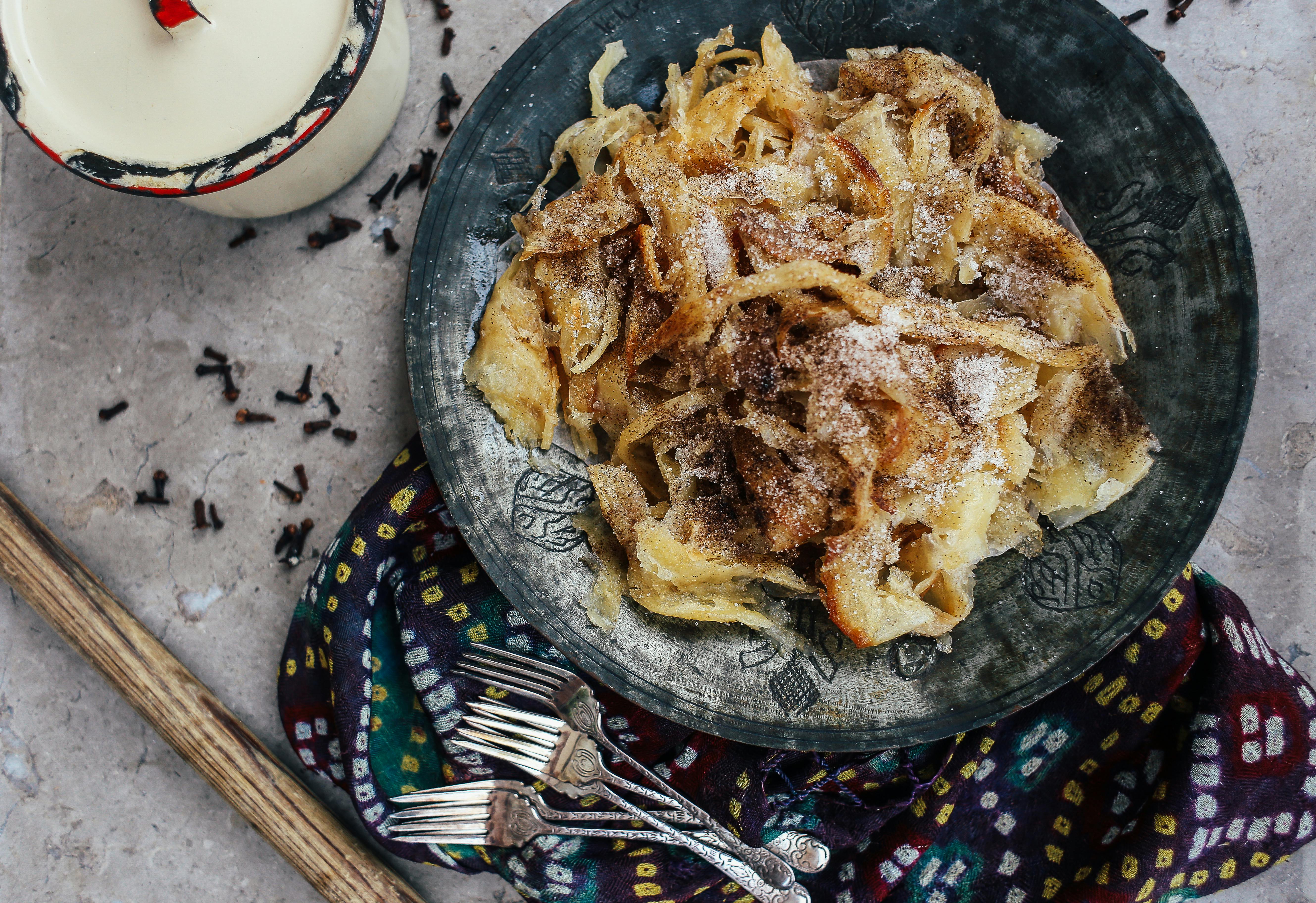 A top view of a rustic, traditional food dish on a black plate, styled with forks and spices.