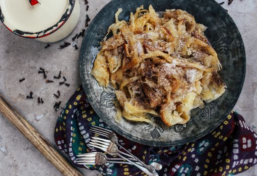 A top view of a rustic, traditional food dish on a black plate, styled with forks and spices.