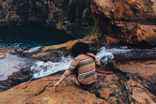 Free A person in colorful attire sits near a waterfall in a rocky canyon, enjoying the outdoors. Stock Photo