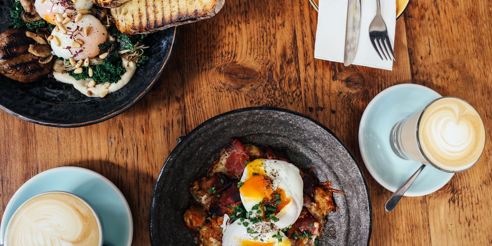 A brunch spread with poached eggs and lattes on a wooden table