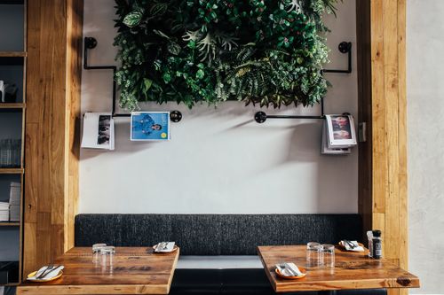 Free Contemporary cafe interior featuring a wooden table, bench seating, and a lush vertical garden. Stock Photo