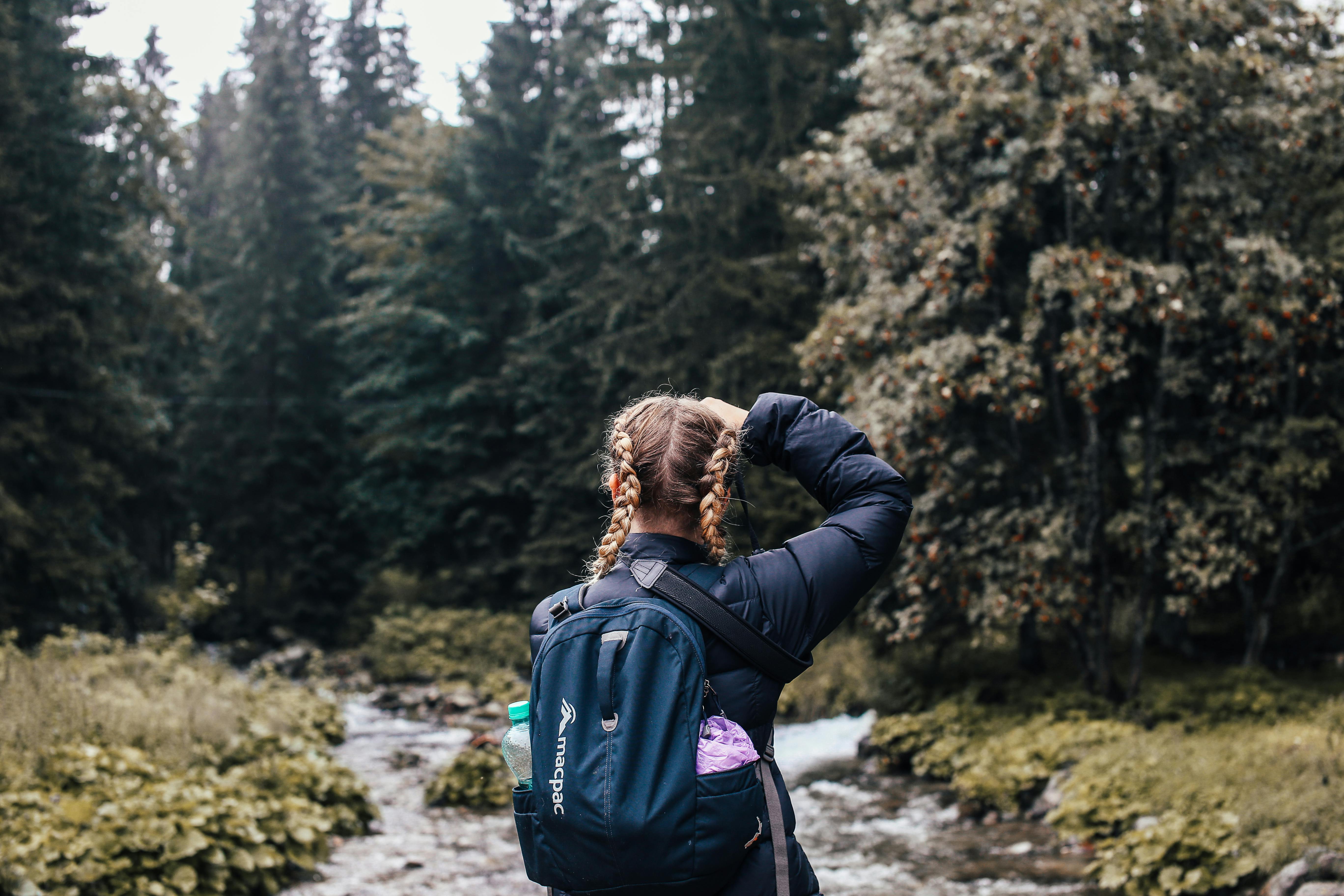 A woman with a backpack hikes along a forest creek, embracing nature and adventure.