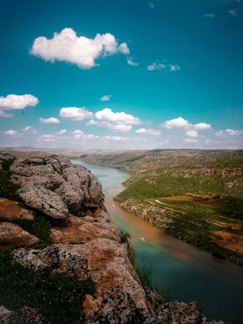 Free Breathtaking scenery of spacious green terrain with rocky formations and calm blue river flowing beneath clear blue sky Stock Photo