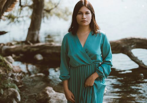 Free Portrait of an elegant brunette woman in a blue dress by a serene lakeside. Stock Photo