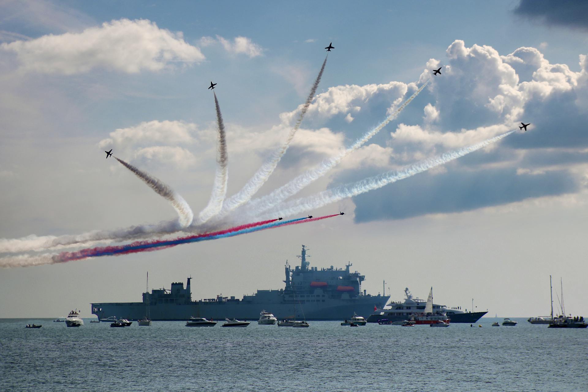 Stunning air display with colored smoke trails above naval ships on a sunny day at sea.