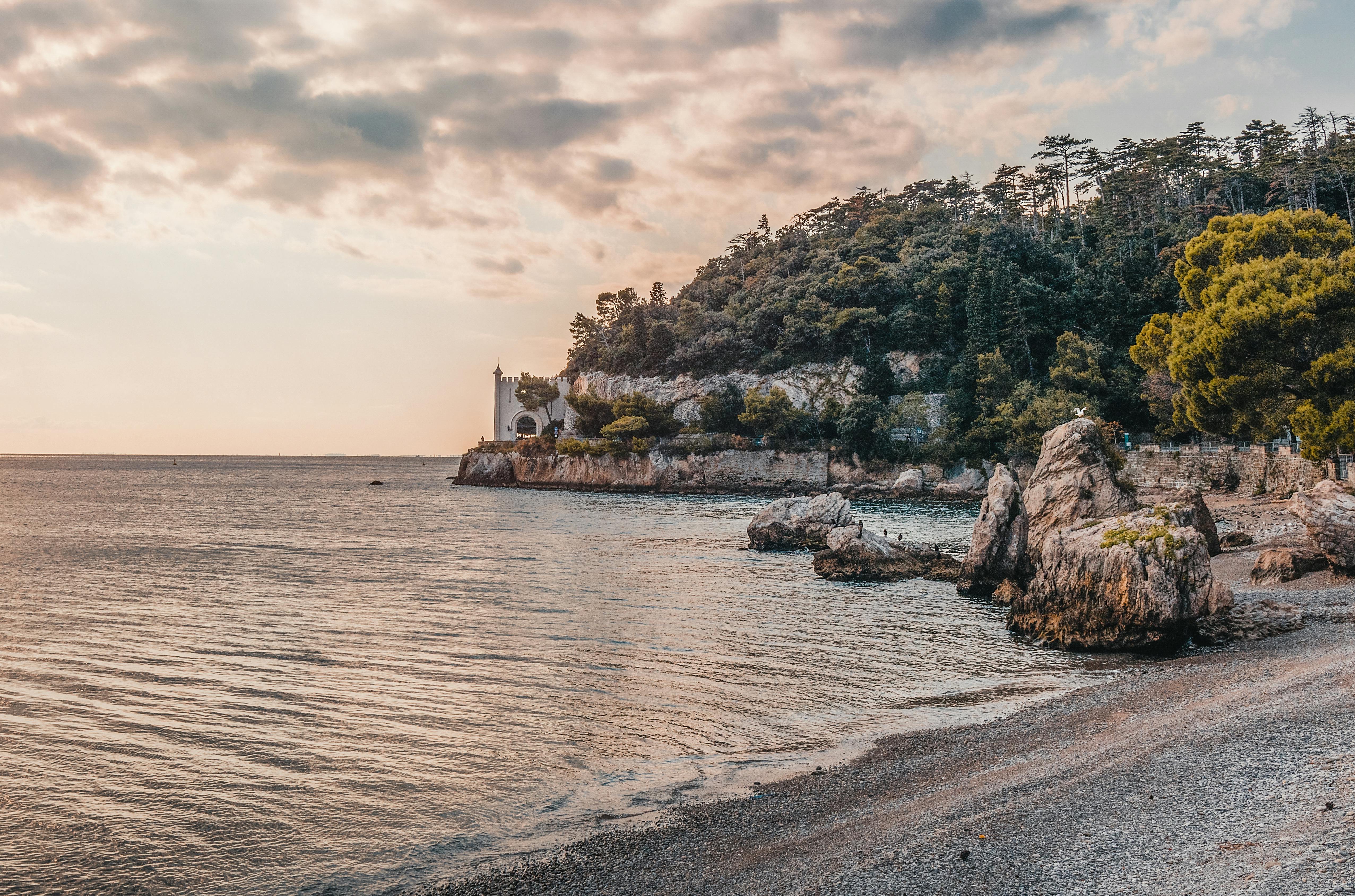 Beautiful coastal landscape featuring a historic castle, rocky shoreline, and serene sea under a vibrant sunset sky.