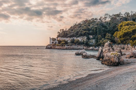 Beautiful coastal landscape featuring a historic castle, rocky shoreline, and serene sea under a vibrant sunset sky.