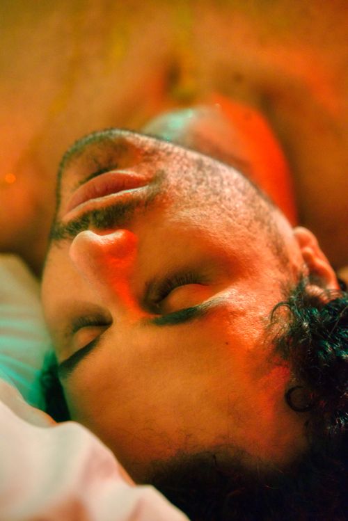 Free A man lying down with eyes closed, illuminated by warm colored lighting, creating a peaceful mood. Stock Photo