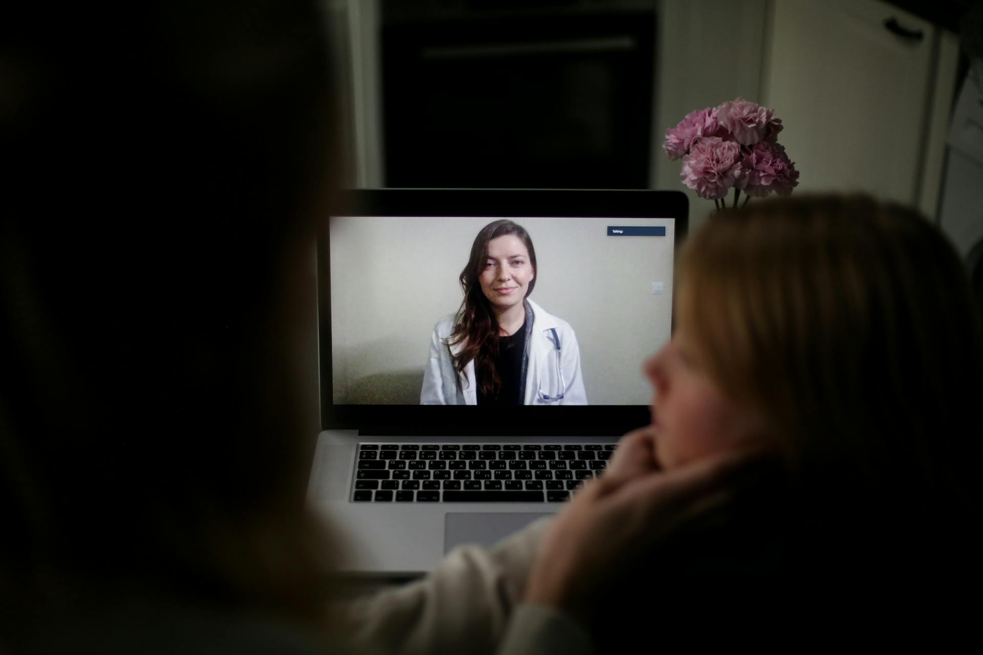 A doctor appears on a laptop screen during an online medical consultation at home.