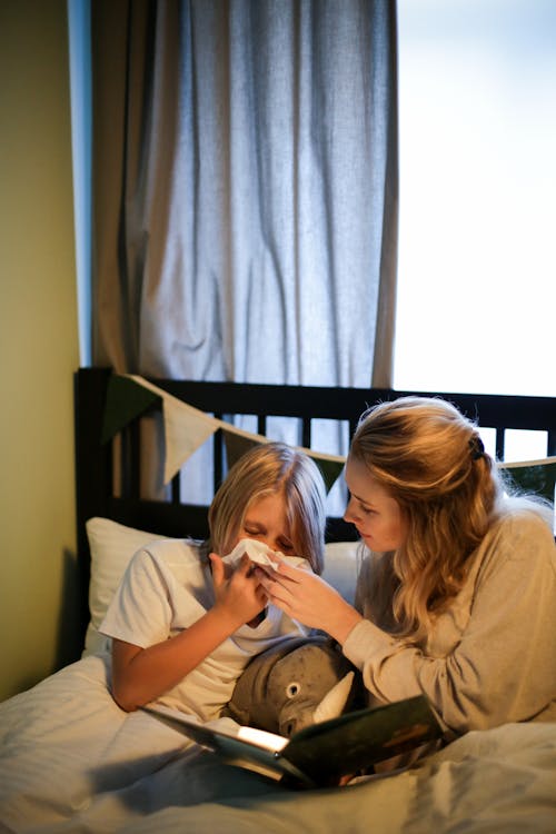 Woman in Beige Shirt Sitting on Bed Beside Woman in White Shirt