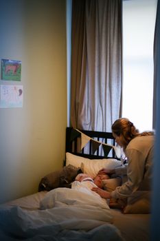 在舒适的卧室里，一位母亲正慈爱地照顾着她年幼的孩子