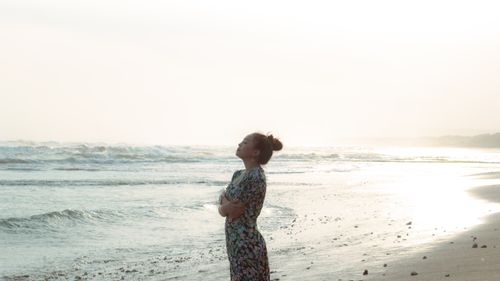 Free A woman enjoys a tranquil moment on a sunny beach with waves in the background. Stock Photo