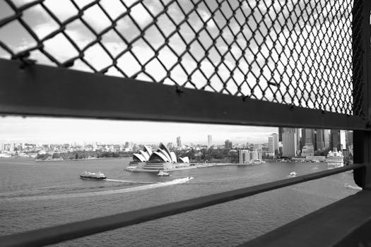 Black and white view of Sydney Opera House through a fence. Iconic Sydney cityscape.