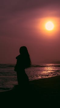 A serene silhouette of a woman standing on a beach during sunset, capturing tranquility and beauty.
