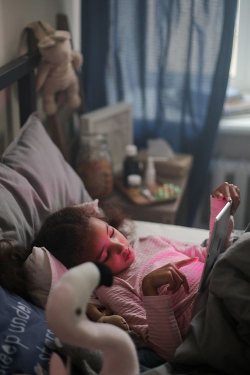 Free A young girl in a cozy bedroom using a tablet, with soft natural light filtering in. Stock Photo