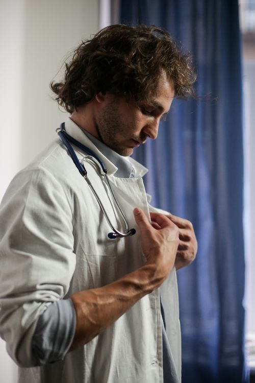 Free Side view of a male doctor adjusting his stethoscope indoors, professional medical scene. Stock Photo