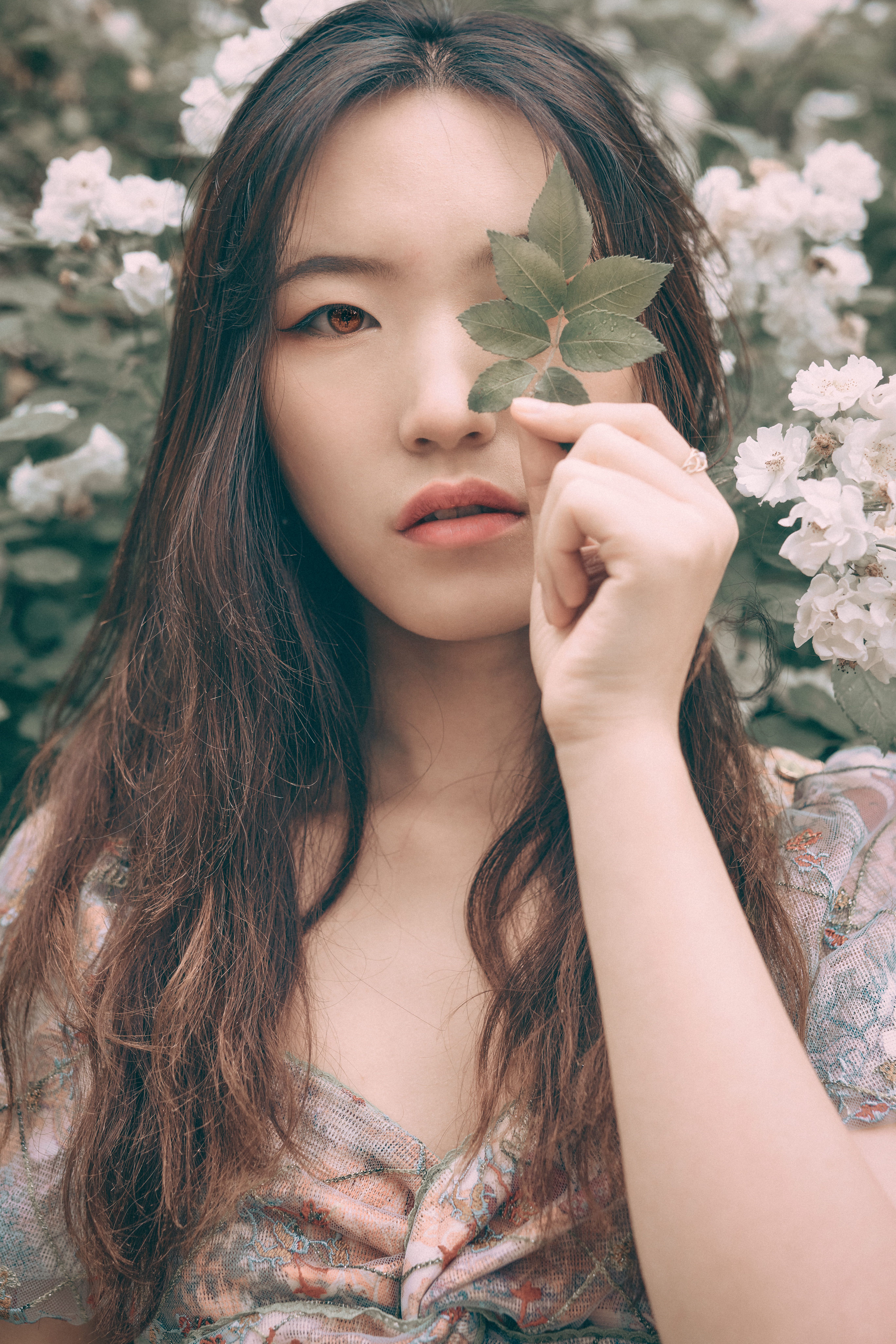 A serene portrait of a woman holding a leaf amidst blooming flowers in a Beijing garden.
