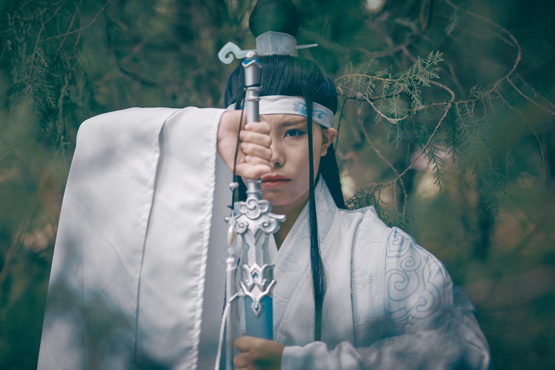 Asian woman in traditional Chinese attire with a sword amidst foliage, Beijing setting.