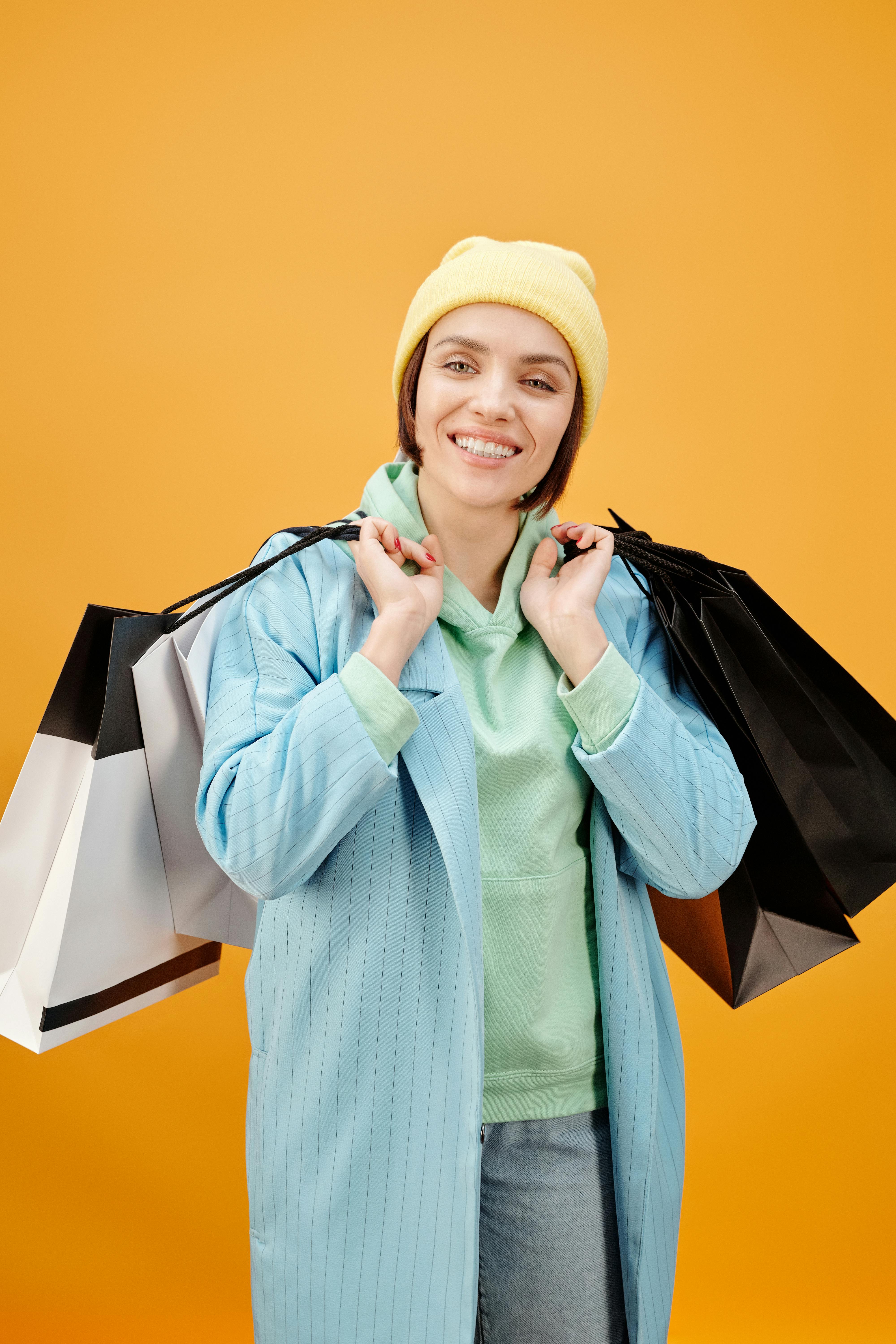 一位开朗的年轻女子在橙色背景前，手持多个颜色鲜艳的购物袋