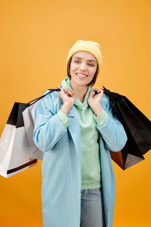 Free Cheerful young woman in vibrant colors holding multiple shopping bags against an orange backdrop. Stock Photo