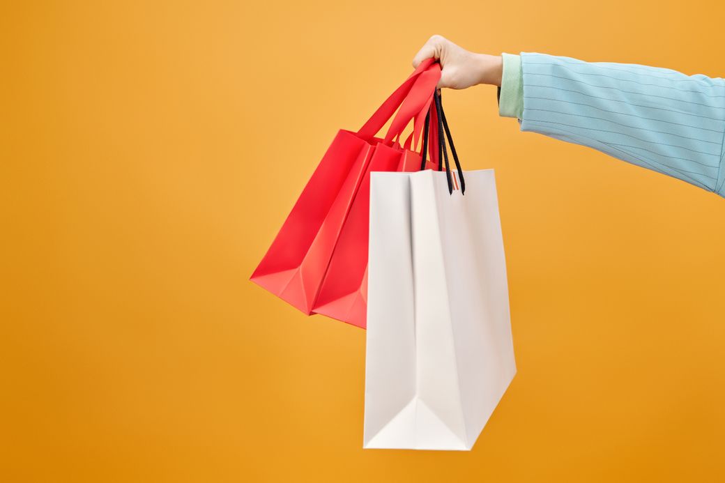 A hand holding paper shopping bags against an amber backdrop — photo by Max Fischer on Pexels