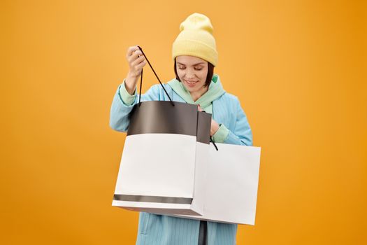 在充满活力的黄色背景上，一位微笑的女人拿着购物袋