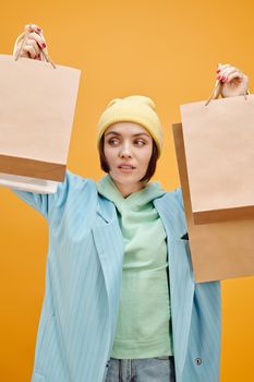 黄色背景下，一位穿着鲜艳服装、拿着购物袋的时尚女子