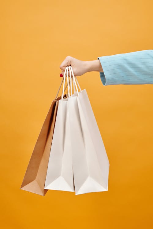 Free A Hand Holding Shopping Bags on a Yellow Background Stock Photo