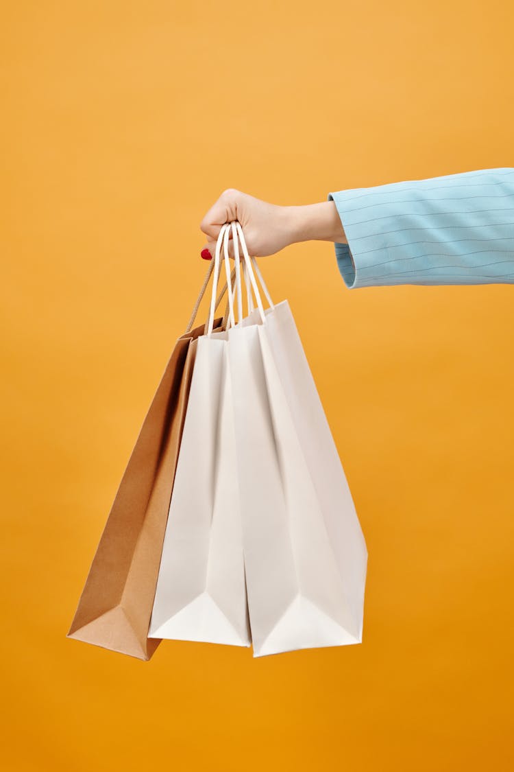 A Hand Holding Shopping Bags On A Yellow Background