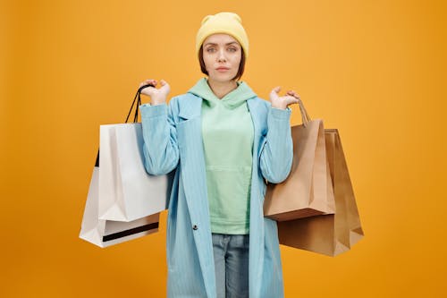 Woman in Teal Coat Carrying Shopping Bags while Seriously Looking at the Camera