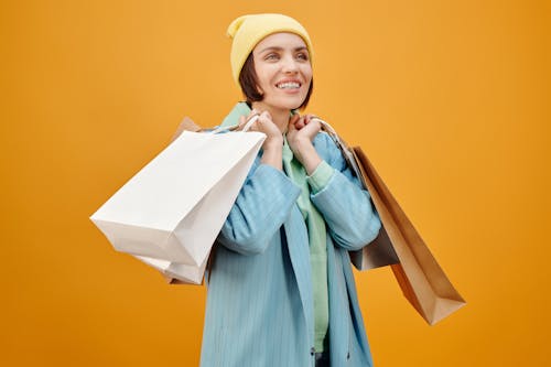 Free Женщина в желтой вязаной шапке и зеленой рубашке с длинным рукавом держит белые бумажные пакеты Stock Photo