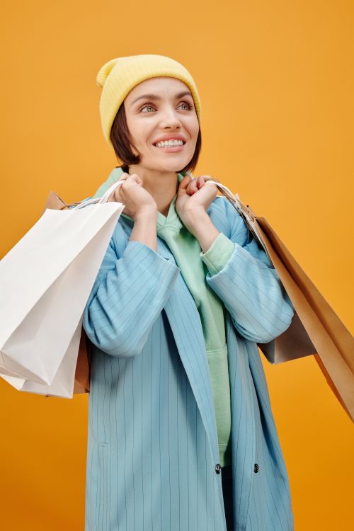 Free Happy woman dressed in vibrant clothing holding shopping bags with a yellow backdrop. Stock Photo