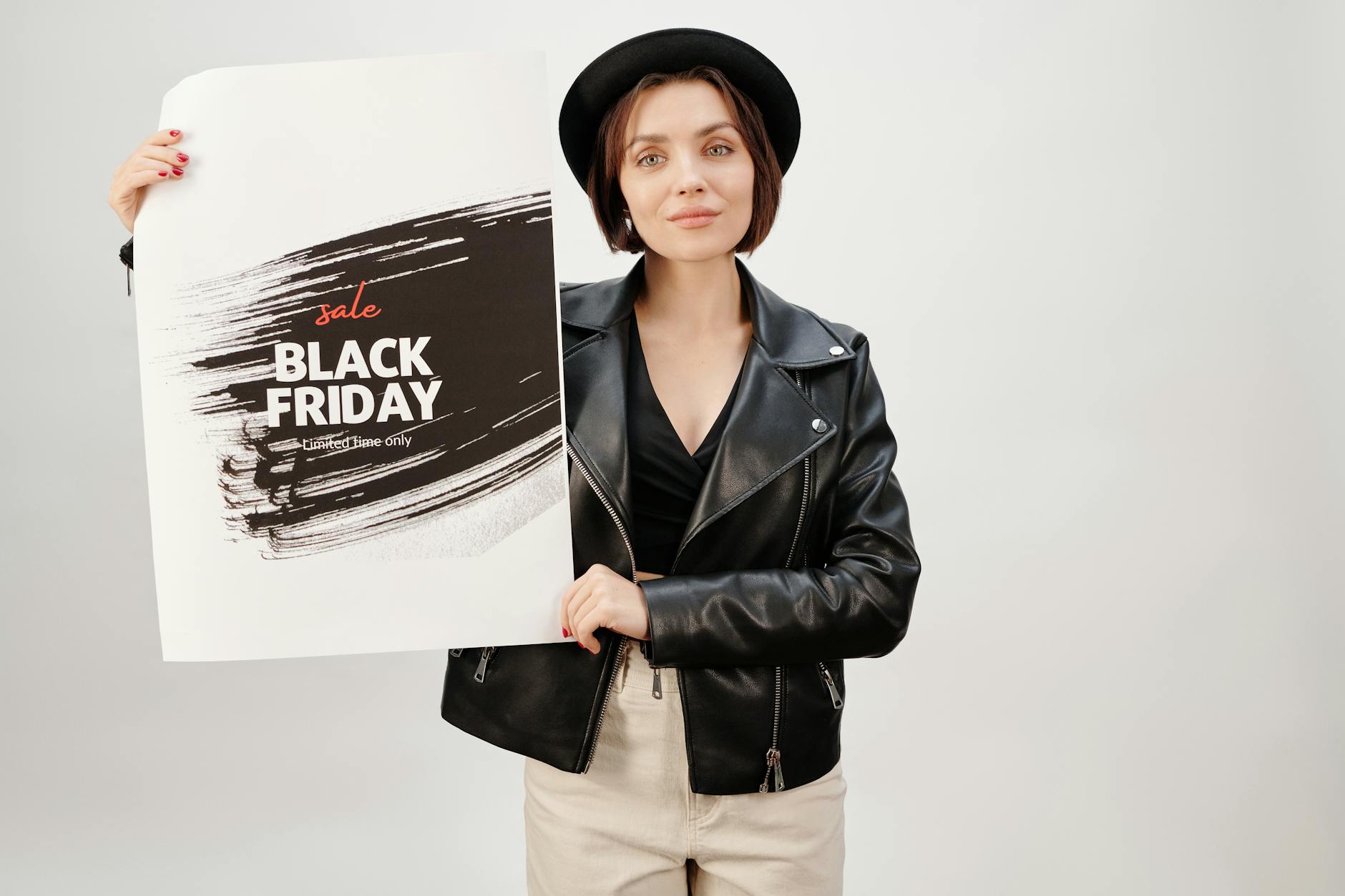 A woman in a leather jacket holding a Black Friday sale poster in a studio setting.