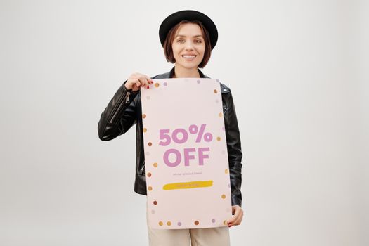 Stylish woman smiling and holding a 50% off sale poster on a white background.