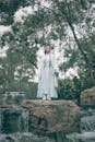 Woman in White Traditional Wear Standing on Brown Rock Holding a Sword
