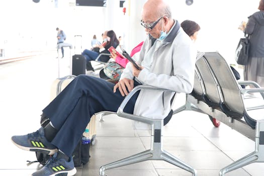 Senior adult using a smartphone in an airport terminal, sitting with luggage nearby.
