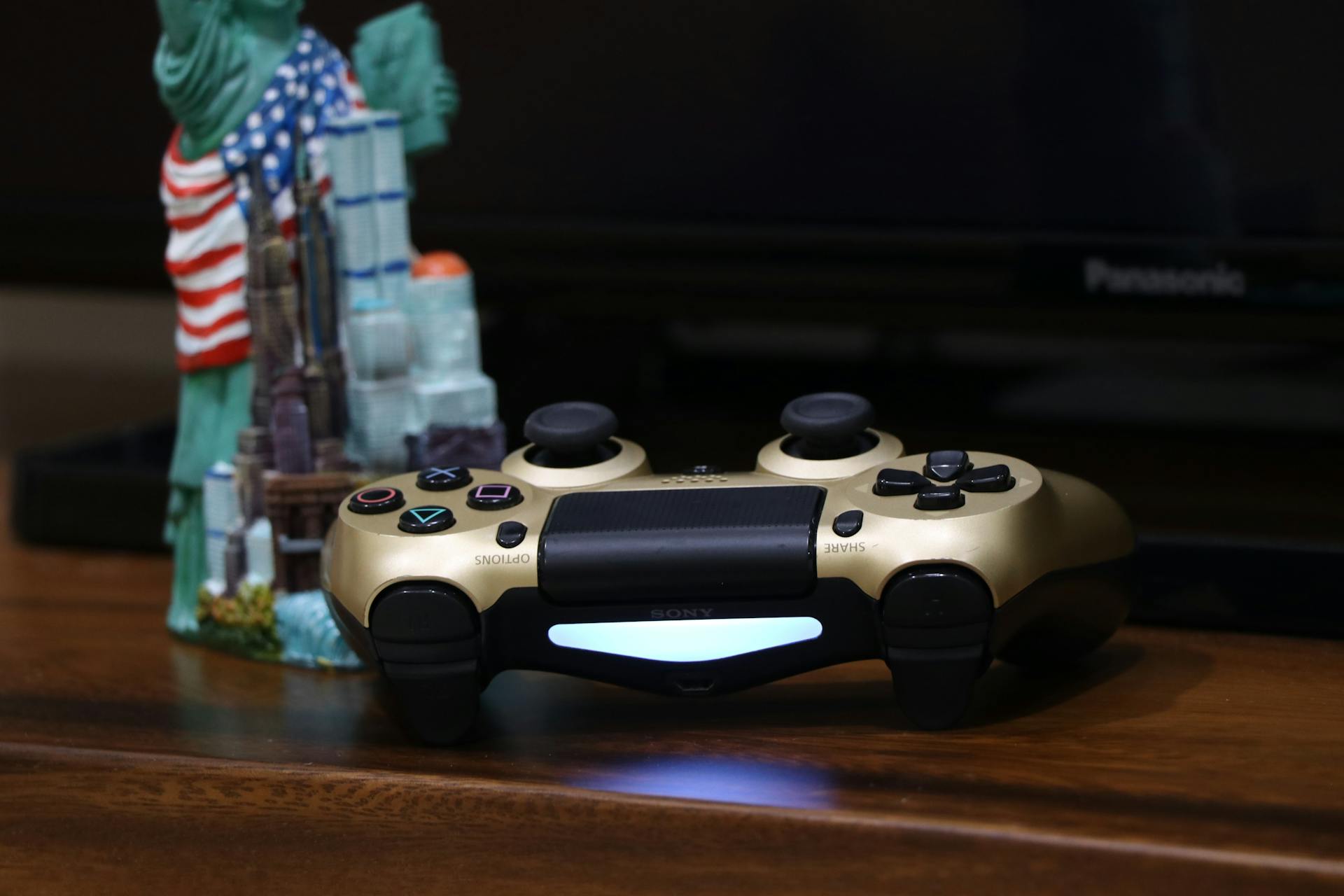 Close-up of a gold PlayStation controller beside a Statue of Liberty figurine, ideal for gaming and decor themes.