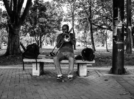 A Man Sitting on Bench while Playing Trombone