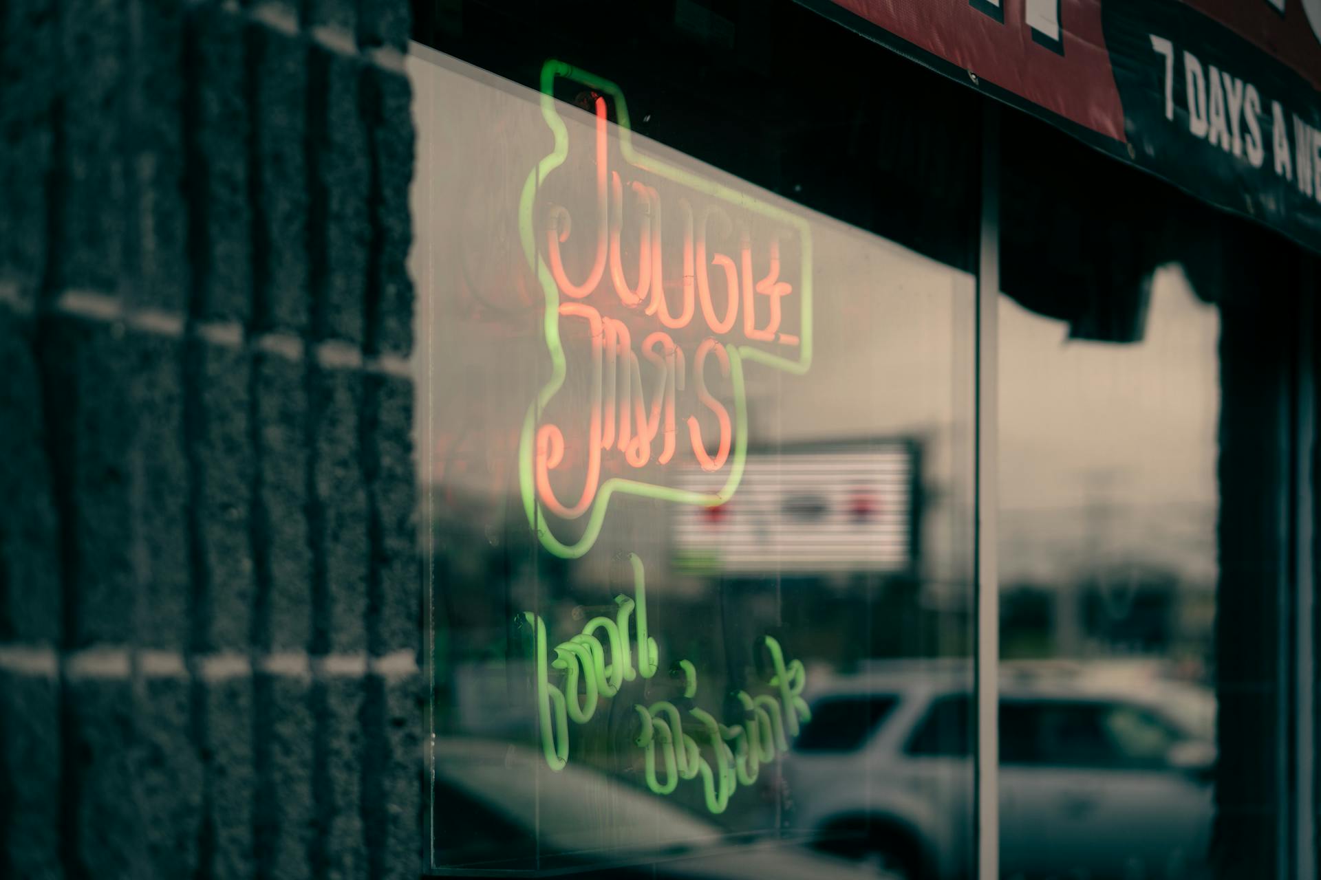 Titles with wavy letters on glass wall of modern building reflecting cars parked on city street in evening