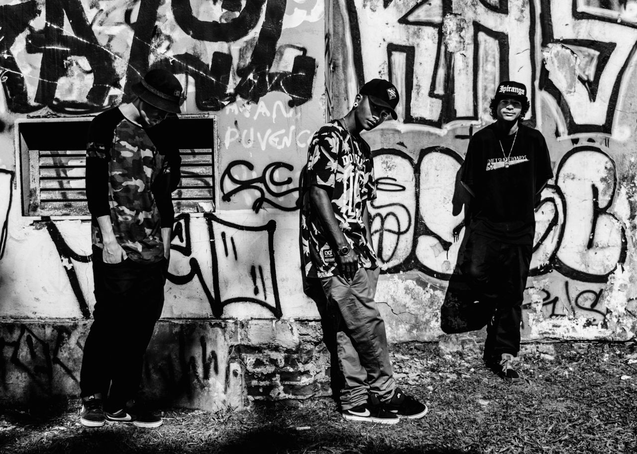 three young adults pose stylishly against a graffiti covered wall in p