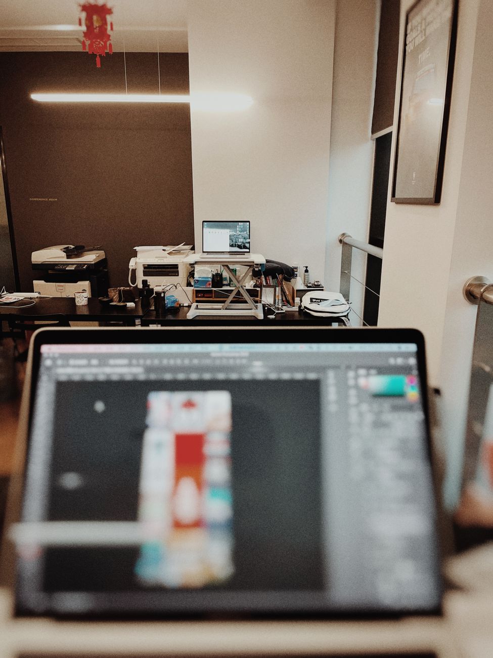 A contemporary office showing a laptop running design software in focus with desks and equipment in the background.