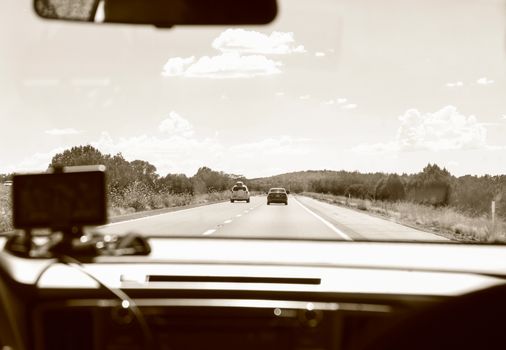 Black and white of car with navigator driving on straight roadway among plants during road trip