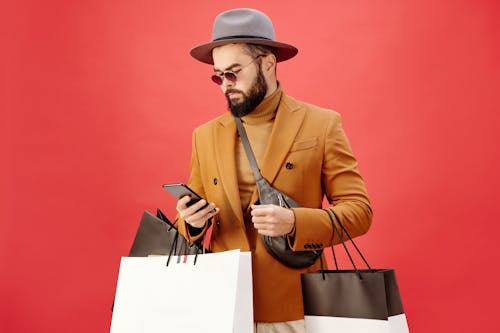 Free Man in a Brown Blazer Carrying Shopping Bags while Using His Cell Phone Stock Photo