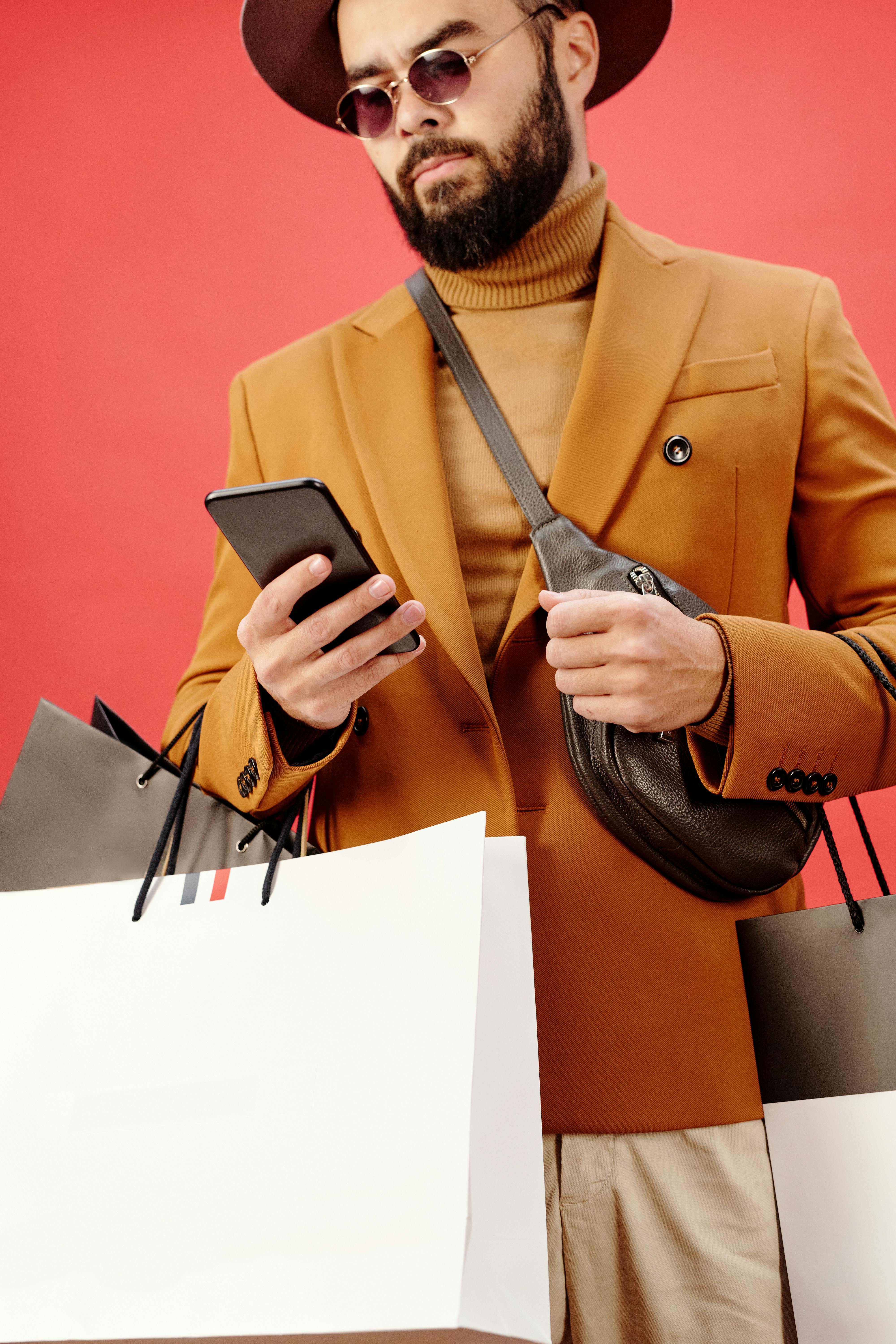 时尚男子在工作室里提着购物袋和智能手机，戴着太阳镜