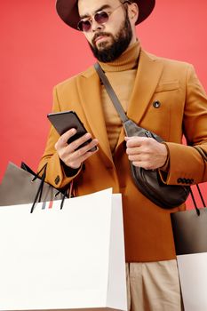 时尚男子在工作室里提着购物袋和智能手机，戴着太阳镜