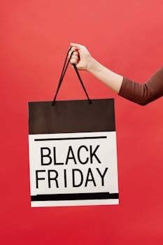 A hand holding a Black Friday shopping bag against a vibrant red background.
