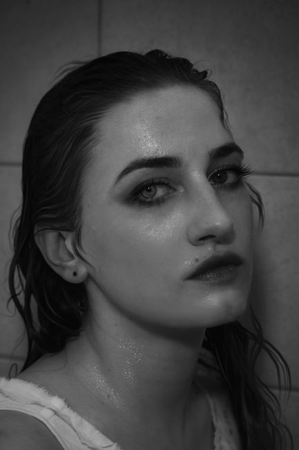 Black and white unemotional sensitive female with wet hair wearing white top looking at camera calmly while standing against tile wall
