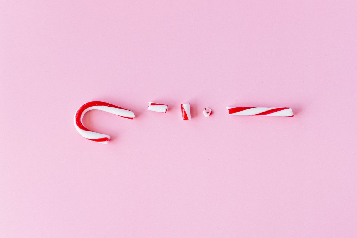 A broken candy cane placed on a vibrant pink background, symbolizing holiday sweetness.