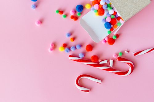 Free Vibrant candy canes and pom poms scattered on a pink background, perfect for festive decor. Stock Photo